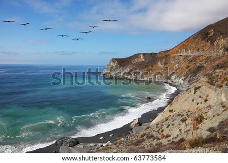 Triangular flight of gray pelicans over rocky coast and azure water of Pacific ocean