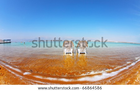Two white beach chairs stood side by side in the clear water. Medical beach on the Dead Sea, Israel