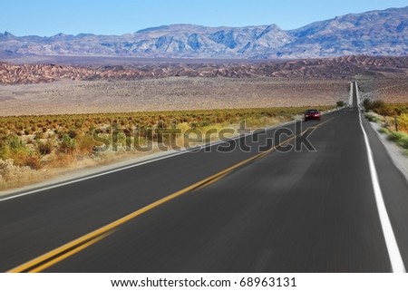 The red car was going at high speed, crossing Death Valley in the USA. The low dry bushes and mountains