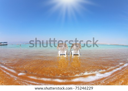 Two white beach armchairs stood side by side in the clear water. Medical beach on the Dead Sea, Israel