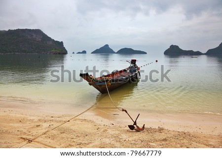 Thai Longtail boat moored on a sandy beach with an anchor. Picturesque bay on the island surrounded by islands