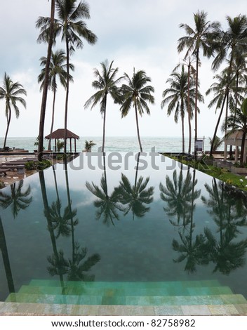 Wide marble steps go down in pool. Smooth water of pool reflects high picturesque palm trees in a beach of Andaman sea