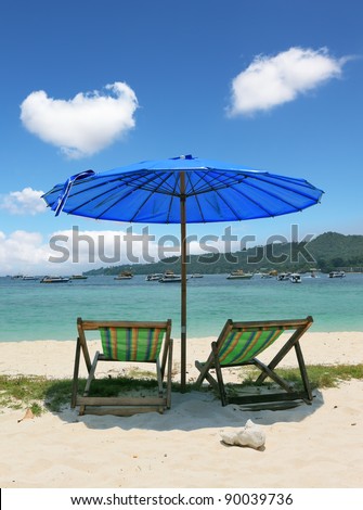 A picturesque dark blue beach umbrella and striped chaise lounges on white beach sand