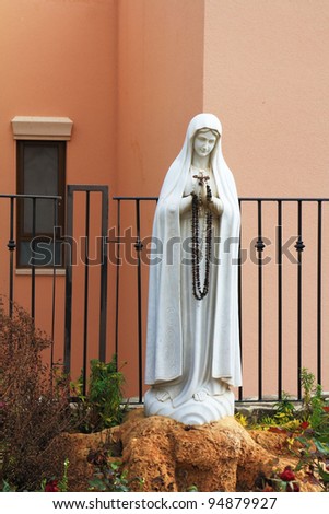 A sculpture of the Virgin Mary with a rosary in his hands. White sculpture.