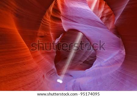 Noon in a red-orange Antelope Canyon. A thin ray of sunlight illuminates the sandy bottom of the canyon