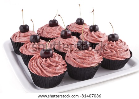 Chocolate flavored cupcakes, with red frosting and a cherry on top, on a white plate on white background
