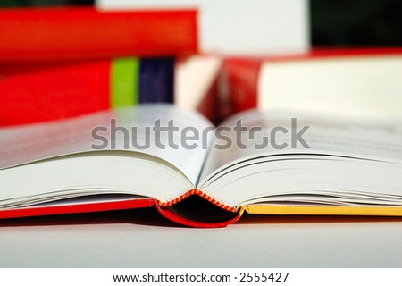 An opened book with pile of books beside it
