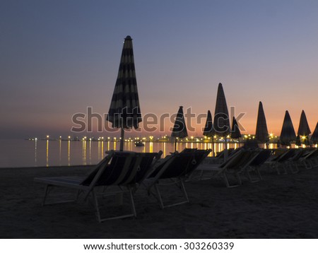 Beach at sunset with beach umbrellas and sun beds -Harbour of Durres / Drach in the background, landscape-Albania