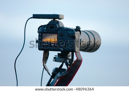 Modern DSLR camera with telephoto lens against soft blue sky