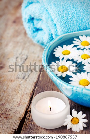 Spa setting with daisies in bowl on wooden background, toned