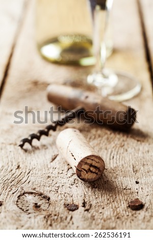 Wine cork and corkscrew on wooden table, wine bottle and glass on the background