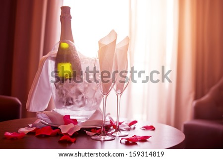 A bottle of Champagne and two glasses with romantic rose petals.