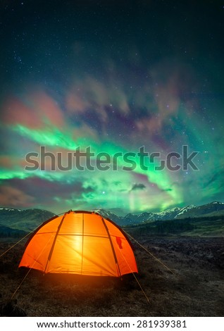 A camping tent glowing under the Northern Lights. Night time camping scene.