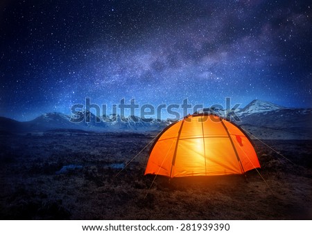 A camping tent glows under a night sky full of stars. Outdoor Camping adventure.