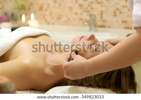 Woman enjoying stone therapy/A female receiving massage and hot rock treatment to back and neck at a beauty salon or day spa facility/ Female Receiving a Relaxing Massage Treatment
