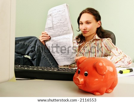 woman in an office reading business statistics of a stock market -with a piggy bank in a foreground
