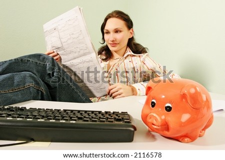 woman in an office reading business statistics of a stock market -with a piggy bank in a foreground