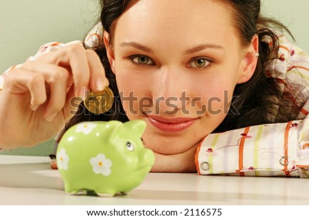 saving money-young woman putting a coin into a green money-box-close up