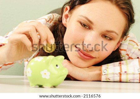 saving money-young woman putting a coin into a green money-box-close up