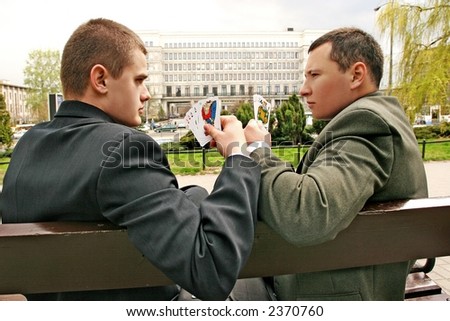 two men playing cards on a street- commercial buildings in the background