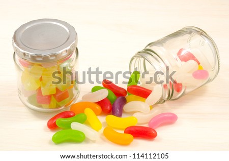 Clear glass jar of candy and colorful jelly beans spilled from jar on wooden board
