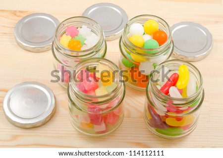 Colorful sweets in the four clear glass jars arranged parallelogram on wooden board