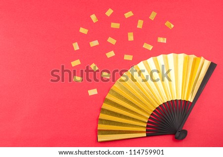 Golden folding fan and golden confetti on red paper