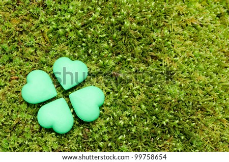 Four green heart shaped objects lined up in form of a clover on the moss