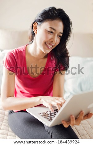 Beautiful Asian Chatting Online with Laptop Lying on Bed in Sunny Summer Day