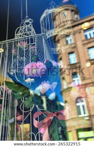Bird cage and a bouquet of flowers in a shop window with a reflection of houses on the street, soft focus