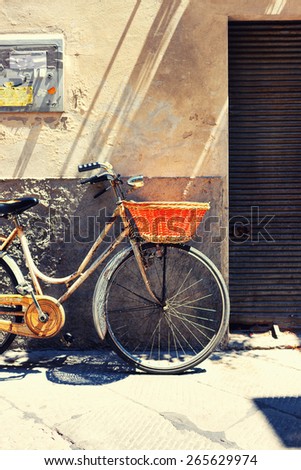 Old bicycle with a basket against the wall advertisement and the entrance to the garage in traditional Tuscany Italy