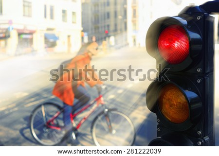 Girl in a red coat on a bicycle at the intersection of the city for a red traffic light in spring day