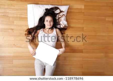 A young adult woman lying on the floor with a blank canvas.