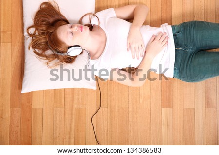 A young redhead girl lying on the floor while listening music.
