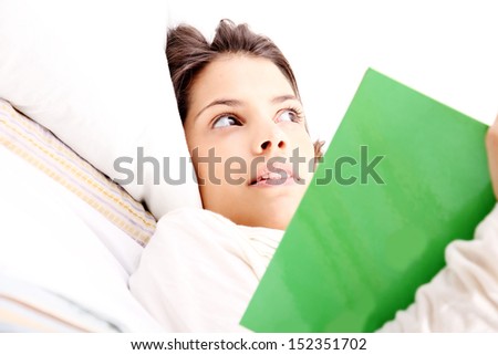 A young latin woman reading a book in bed.