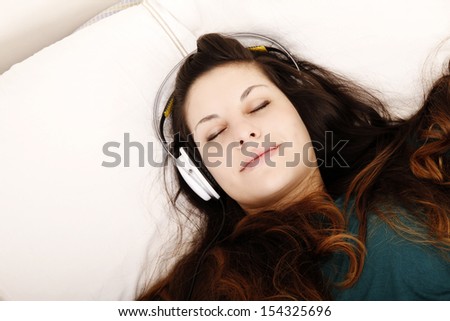 A young adult woman listening music with headphones in bed.