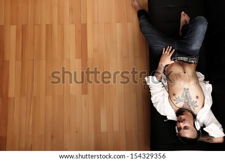 A tattooed hispanic man listening to music while lying on the sofa.