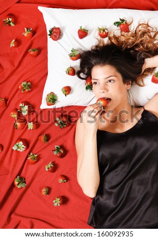 Beautiful, latin Woman eating a Strawberry in bed.