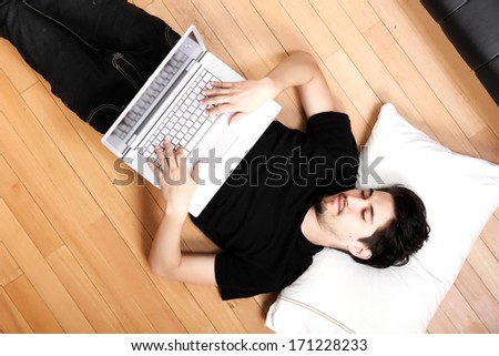 A young hispanic man surfing with a Laptop on the floor.