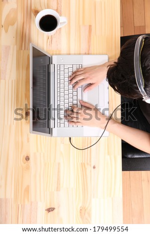 A young hispanic man working on a laptop computer while listening to music with headphones.