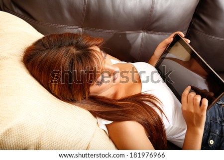 A young woman using a Tablet PC while laying on the sofa.