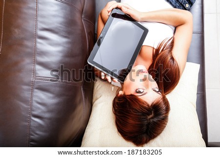A young woman showing a Tablet PC while laying on the sofa.