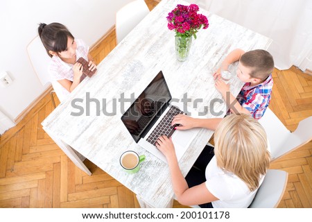 A mother working at home with a laptop and parenting her two children.
