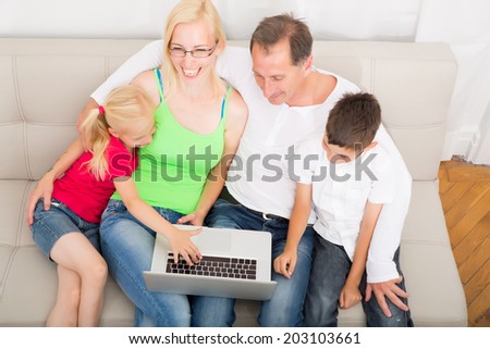 Father and mother with son and daughter on the sofa while using a laptop.
