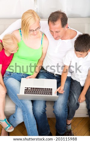 Father and mother with son and daughter on the sofa while using a laptop.