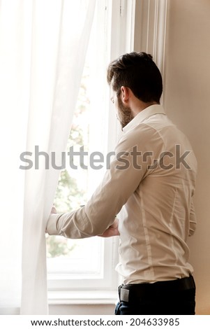 A young adult man looking out the window.