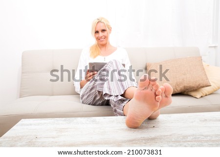 A mature woman in Pyjamas with a Tablet PC on the Sofa. Focus on the Toes.