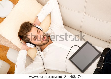 A young handsome man on the couch listening to music.
