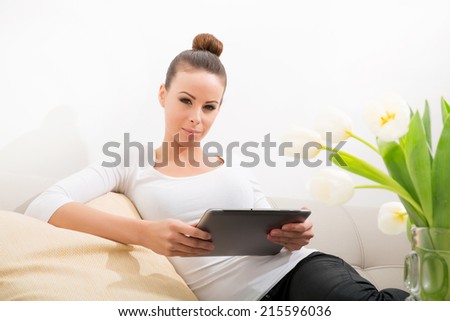 A young woman sitting on the sofa holding a tablet.