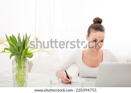 A young adult woman drawing an architectural plan at home with laptop and flowers.